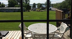 A patio with a round table and chairs, overlooking a grassy yard and a lake. - Muskey's Landing Resort (Tay)