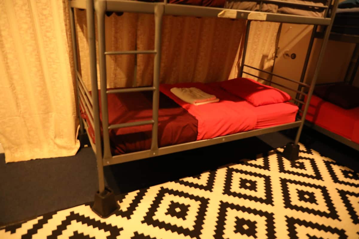A bunk bed with a red mattress and pillows, a patterned rug, and a curtain.