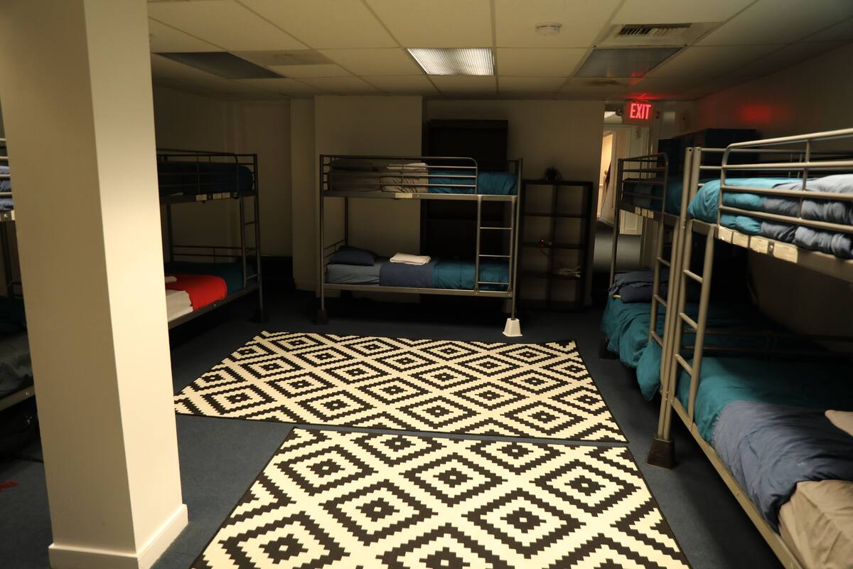 A dormitory room with bunk beds, a patterned carpet, and an exit sign.