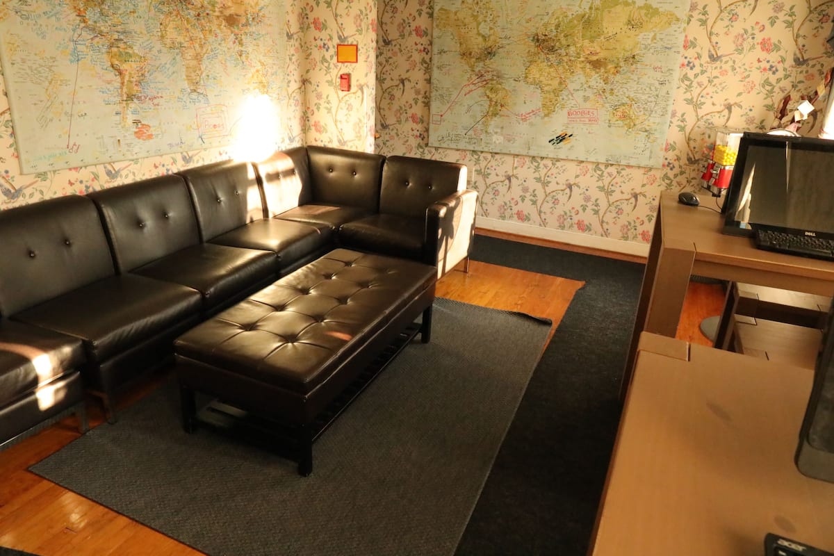 A living room with a sectional sofa, a wooden coffee table, a map-covered wall, and a desk with a computer.
