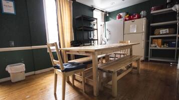 A kitchen with a wooden table and chairs, a refrigerator, and shelves with kitchen items.
