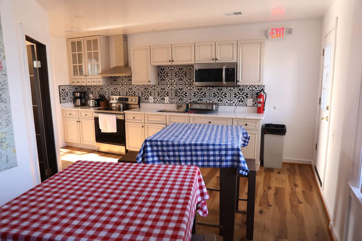 A kitchen with white cabinets, a microwave, and two tables with checkered tablecloths.