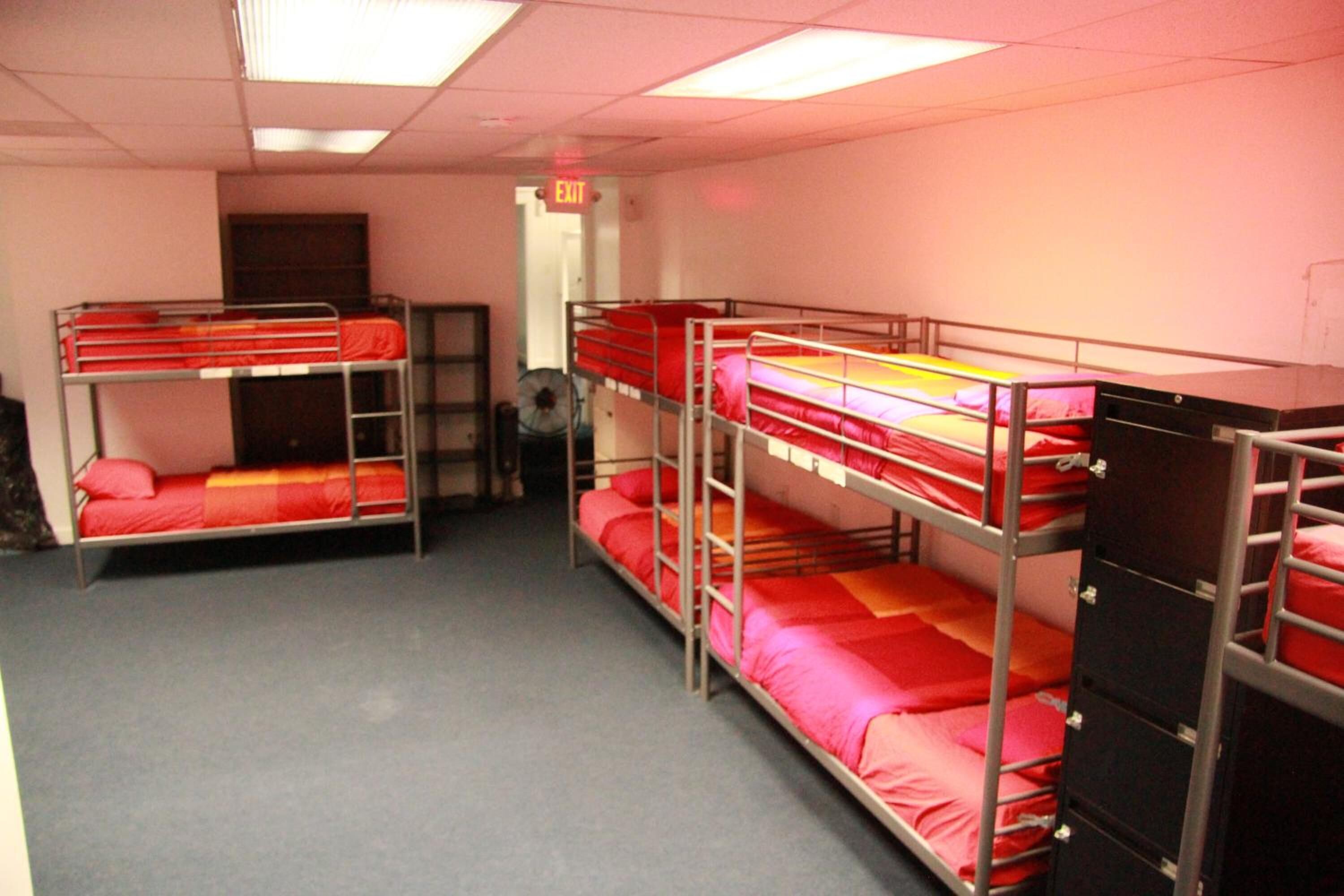 A dormitory room with bunk beds, an exit sign, and a fan.