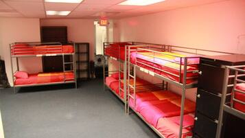 A dormitory room with bunk beds, an exit sign, and a fan.