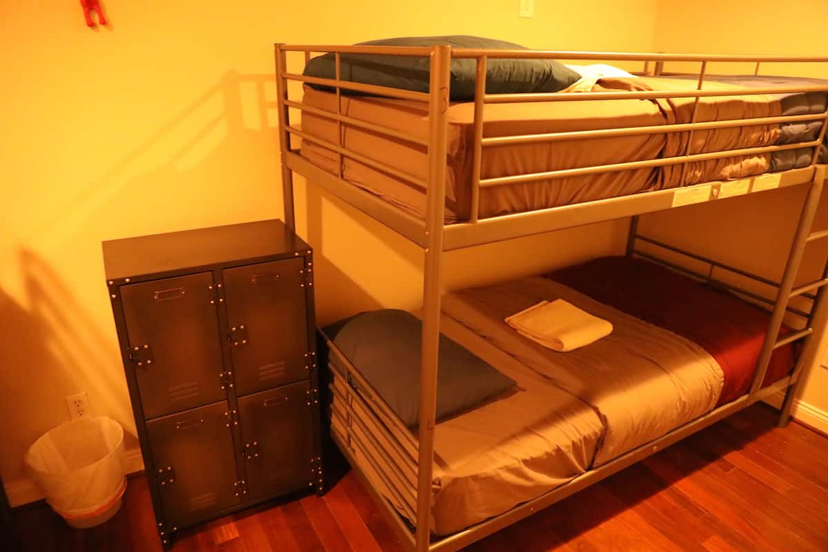 A bunk bed with a storage cabinet and a trash bin in a room with wooden flooring.