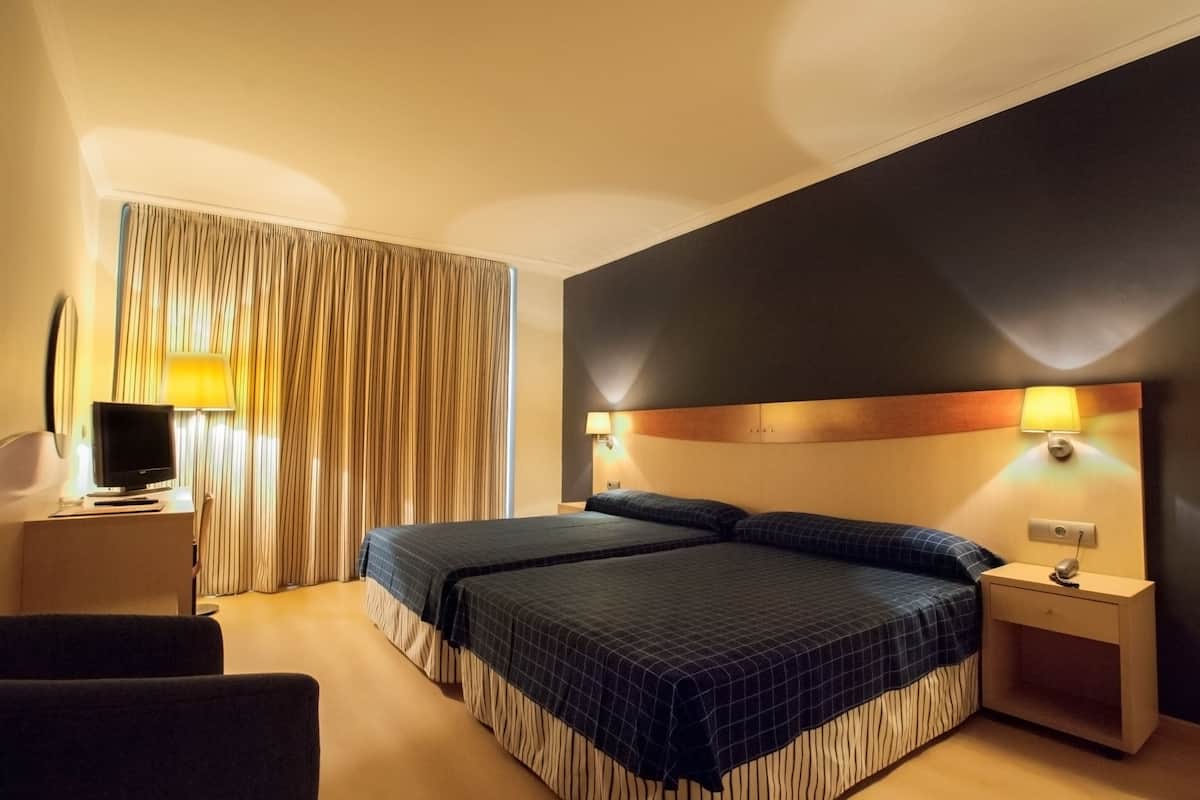 A hotel room with two beds, a desk with a computer, and a chair.