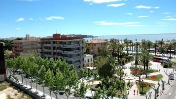 Una zona urbana costera con edificios de varios pisos, un paseo marítimo bordeado de palmeras y vista al mar.