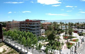 A coastal urban area with multi-story buildings, a promenade lined with palm trees, and a view of the sea. - Evenia President Hotel (Salou)