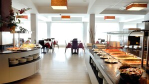 A buffet area with multiple food stations, a seating area with tables and chairs, and a large window providing natural light. - Evenia President Hotel (Salou)