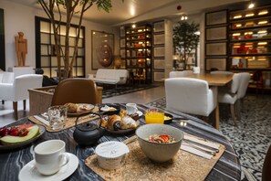 A breakfast setting with a marble table, white chairs, and a variety of breakfast items including croissants, fruit, and a bowl of cereal. - Margot House (Barcelona)