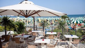 A beachside café with outdoor seating, umbrellas, and a view of the sea. - Hotel Columbia & Ninfea (Jesolo)