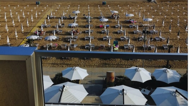 A beach with rows of umbrellas and lounge chairs, a pier extending into the sea, and a clear view of the ocean. - Hotel Columbia & Ninfea (Jesolo)