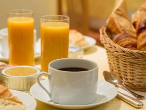 Ein Frühstückstisch mit einer Kaffeetasse, zwei Orangensaftgläsern, Croissants und einem Korbwannenkorb.