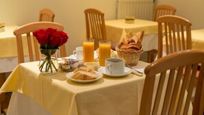 A breakfast table set with croissants, orange juice, coffee, and red roses. - Hôtel Le Home (Vincennes)