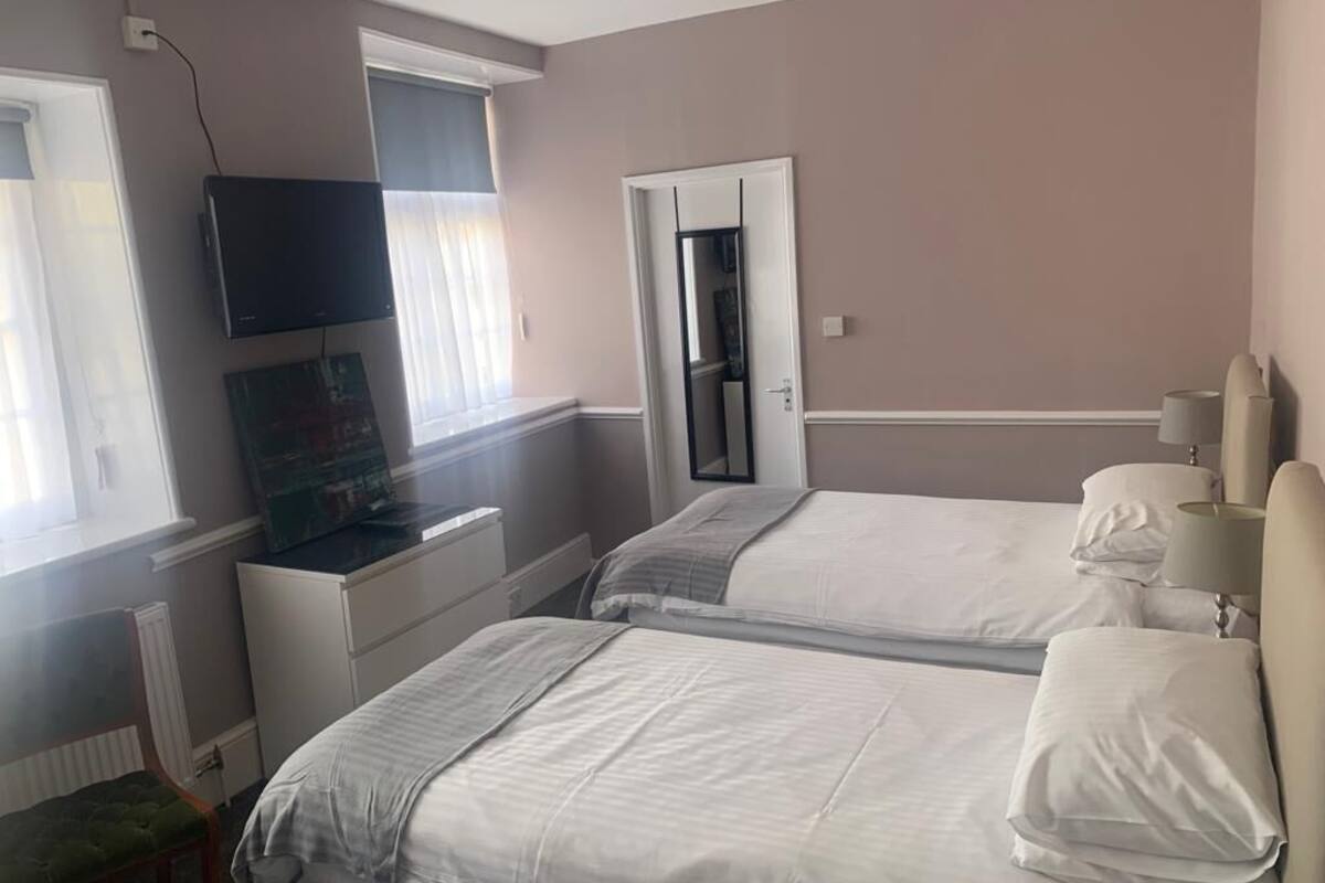 A hotel room with two beds, a television, a window with blinds, and a door leading to a closet.