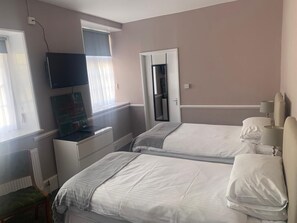 A hotel room with two beds, a television, a window with blinds, and a door leading to a closet. - The Castle Inn (Minehead)