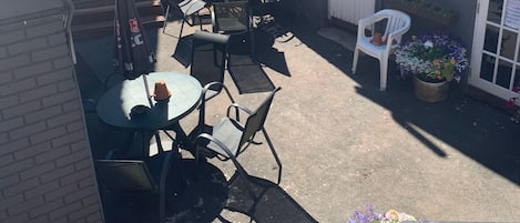 An outdoor patio area with a round table and chairs, a small white chair, and a hanging flower pot.