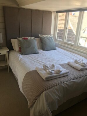 A neatly made bed with pillows, a bedside table, and a window with a view of buildings.