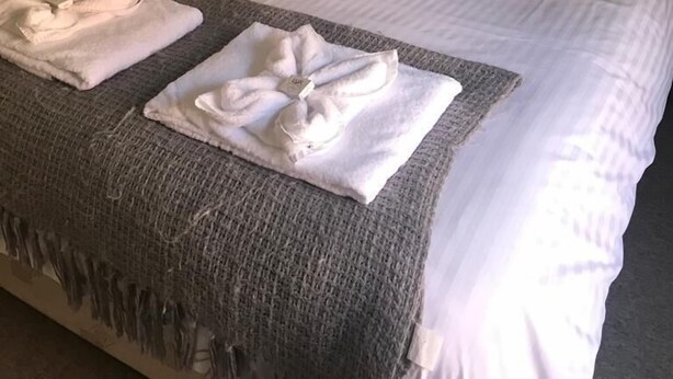 Una cama bien tendida con sábanas blancas y dos toallas dobladas sobre una manta gris.