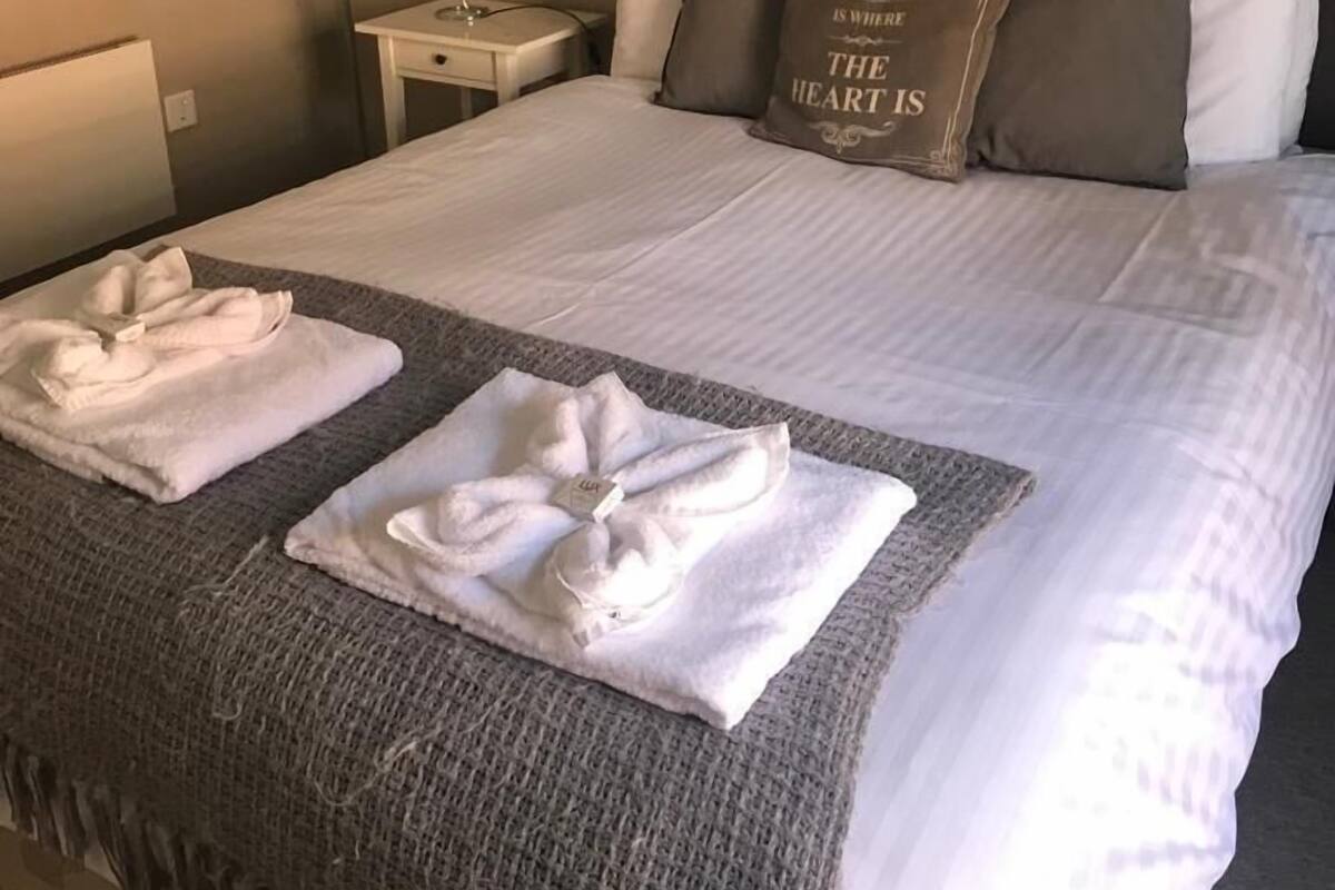 A neatly made bed with white linens and two towels folded on a gray blanket.