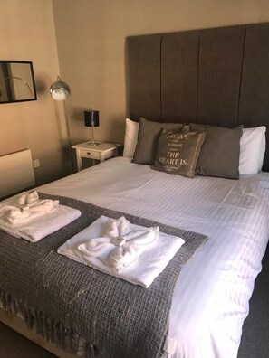 A neatly made bed with white linens and two towels folded on a gray blanket. - The Castle Inn (Minehead)