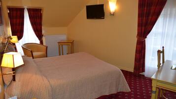 A hotel room with a bed, a chair, a small table, a lamp, a TV, and a window with curtains.