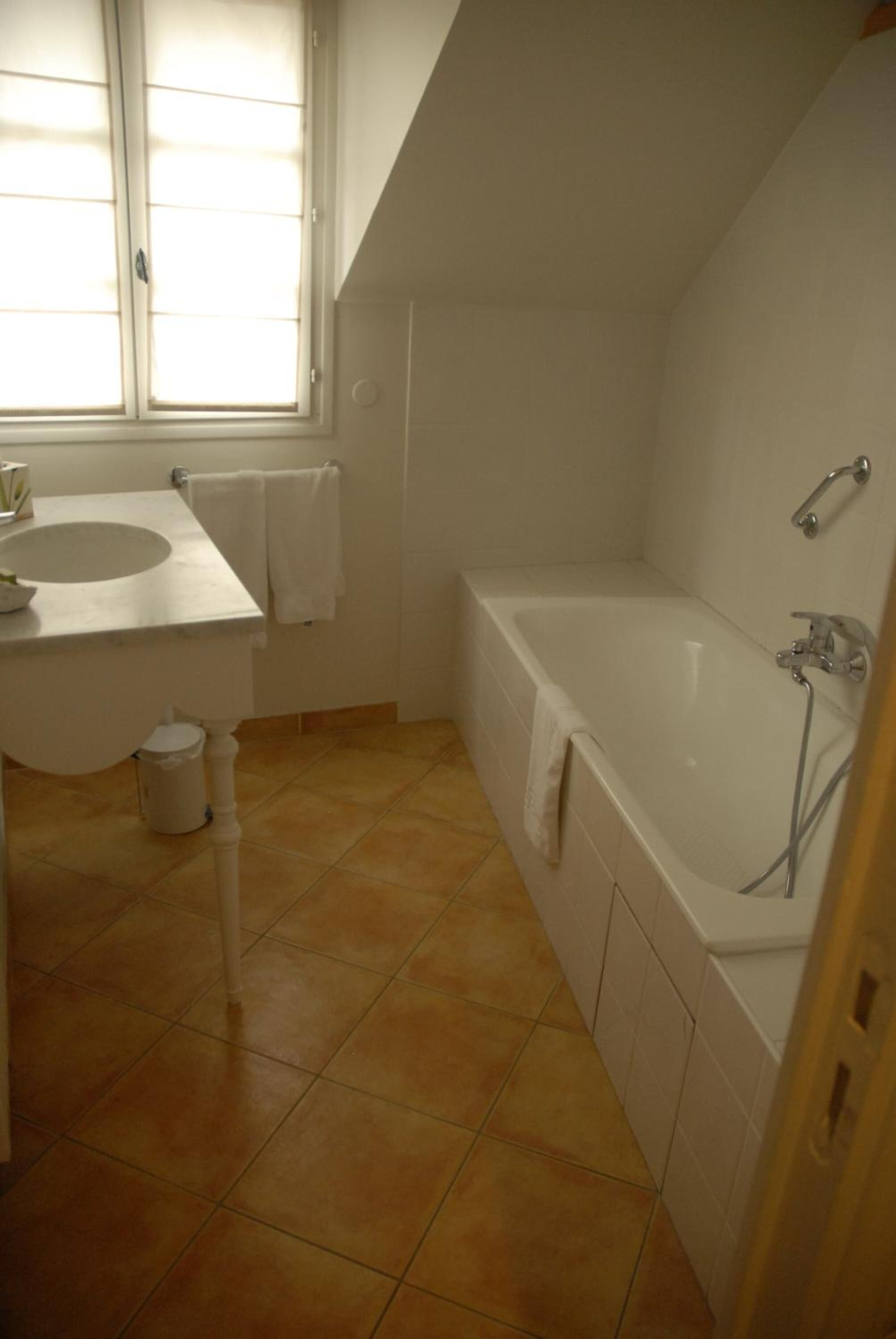 Une salle de bain avec un lavabo blanc, une baignoire et une fenêtre.