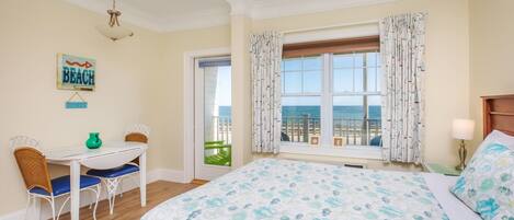 Ein Schlafzimmer mit einem großen Bett, einem Schreibtisch mit Stühlen, Meerblick durch ein Fenster und einem Schild im Strandhaus-Stil an der Wand.