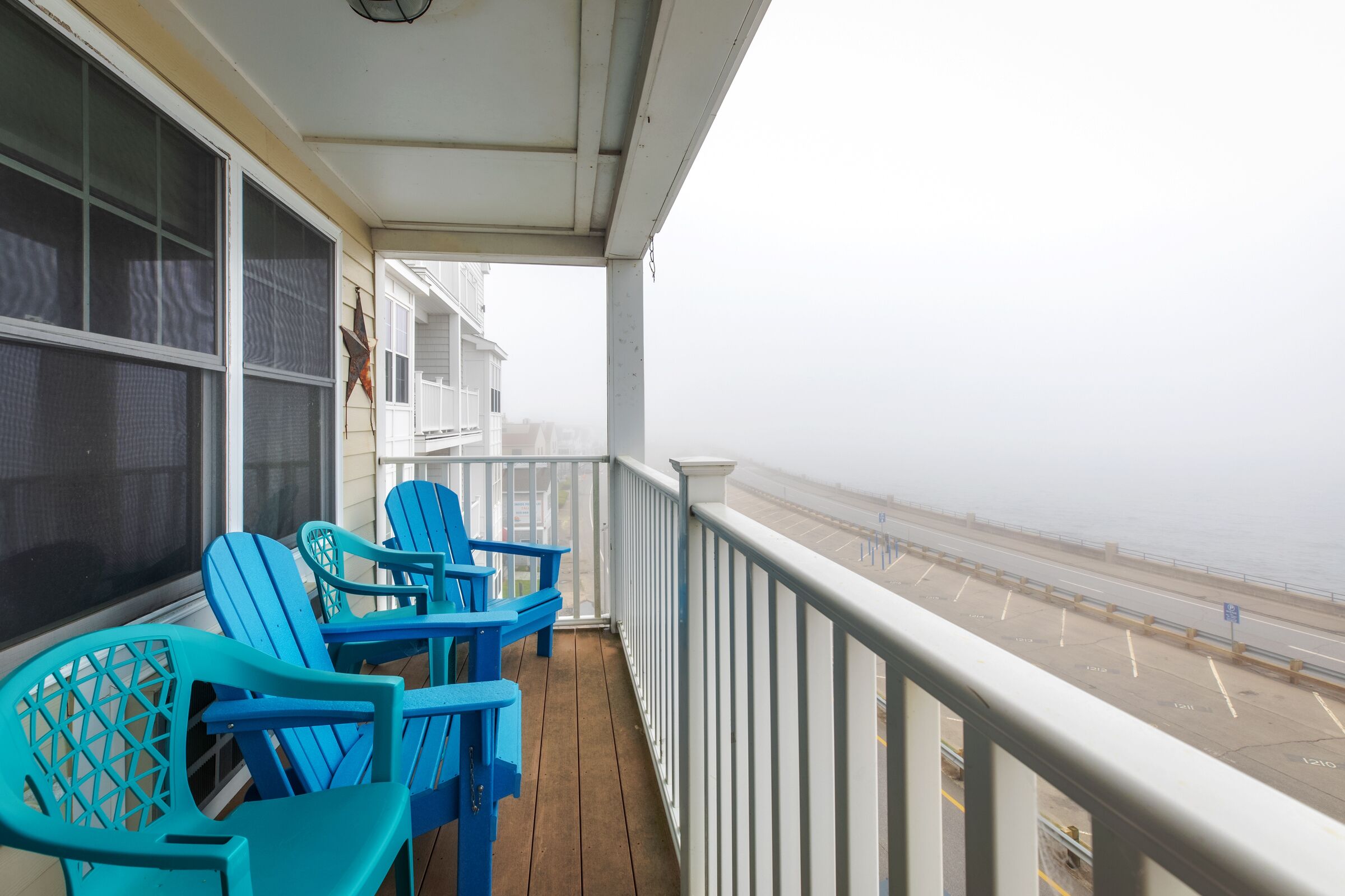 A balcony with blue Adirondack chairs, a white railing, and a view of the beach.