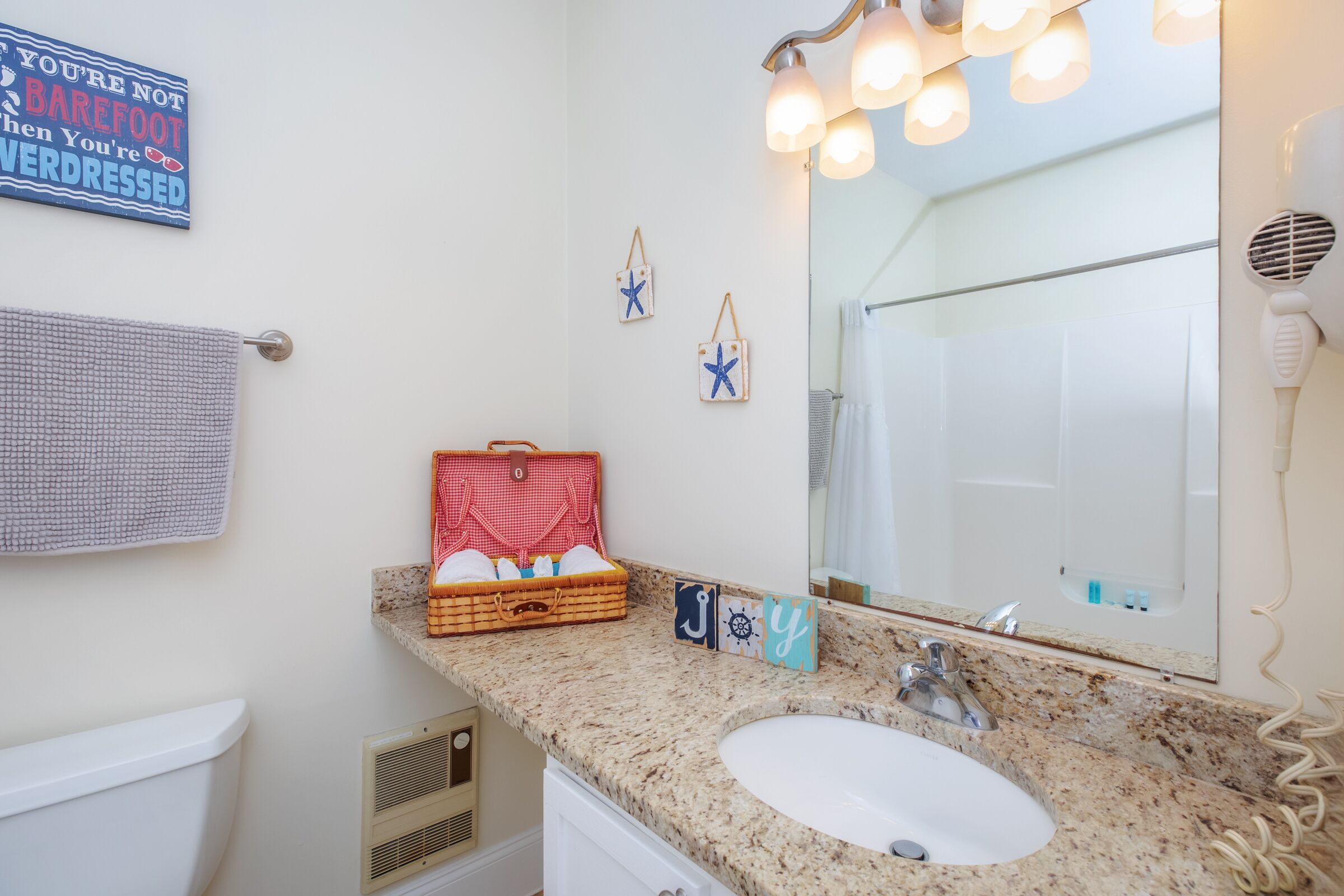 A bathroom with a white sink, a mirror with lights, a towel rack, and a red suitcase on the counter.