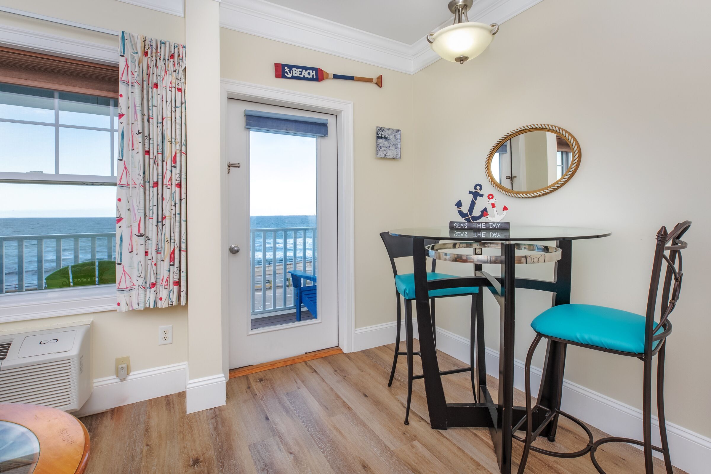 Une pièce avec vue sur la mer, une table avec des chaises, un miroir et un panneau accroché au mur.