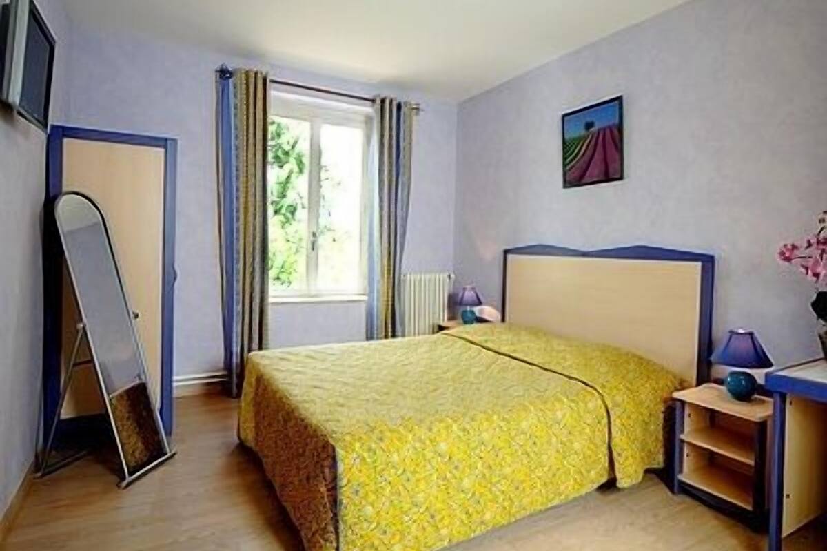 Une chambre à coucher avec un lit, un bureau, une chaise, un miroir et une fenêtre avec des rideaux.