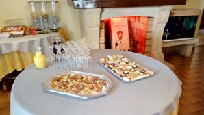 Une table ronde recouverte d’une nappe blanche, deux plateaux rectangulaires remplis de nourriture, une bouteille de moutarde et plusieurs verres.