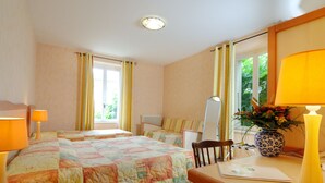 Une chambre d’hôtel avec deux lits, un bureau, une chaise, une lampe, un vase avec des fleurs et une fenêtre avec des rideaux.