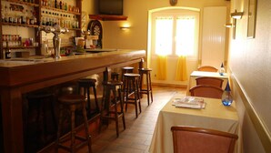 Un espace bar avec des tabourets, un comptoir avec des bouteilles, un jeu de fléchettes et un téléviseur fixé au mur.