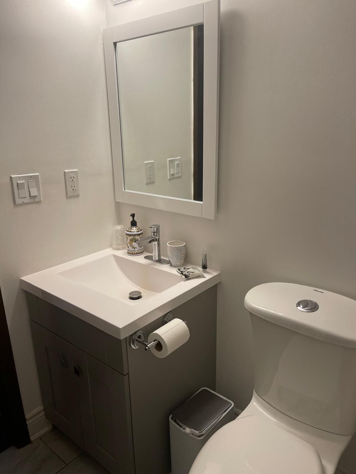 A bathroom with a white sink, mirror, toilet, and a trash bin.