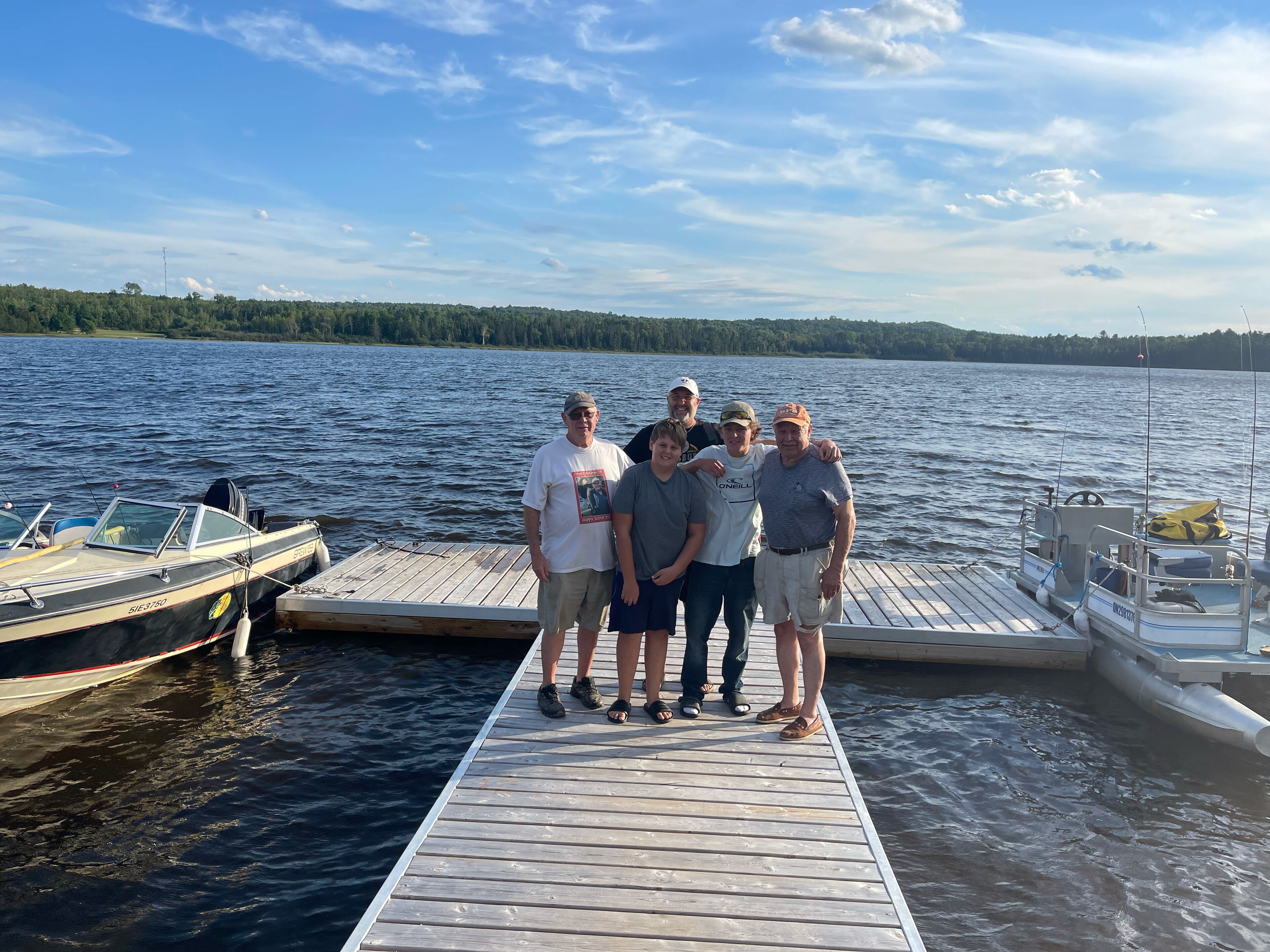 Un groupe de personnes se tient sur une jetée en bois, au bord d’un lac, avec des bateaux à proximité.