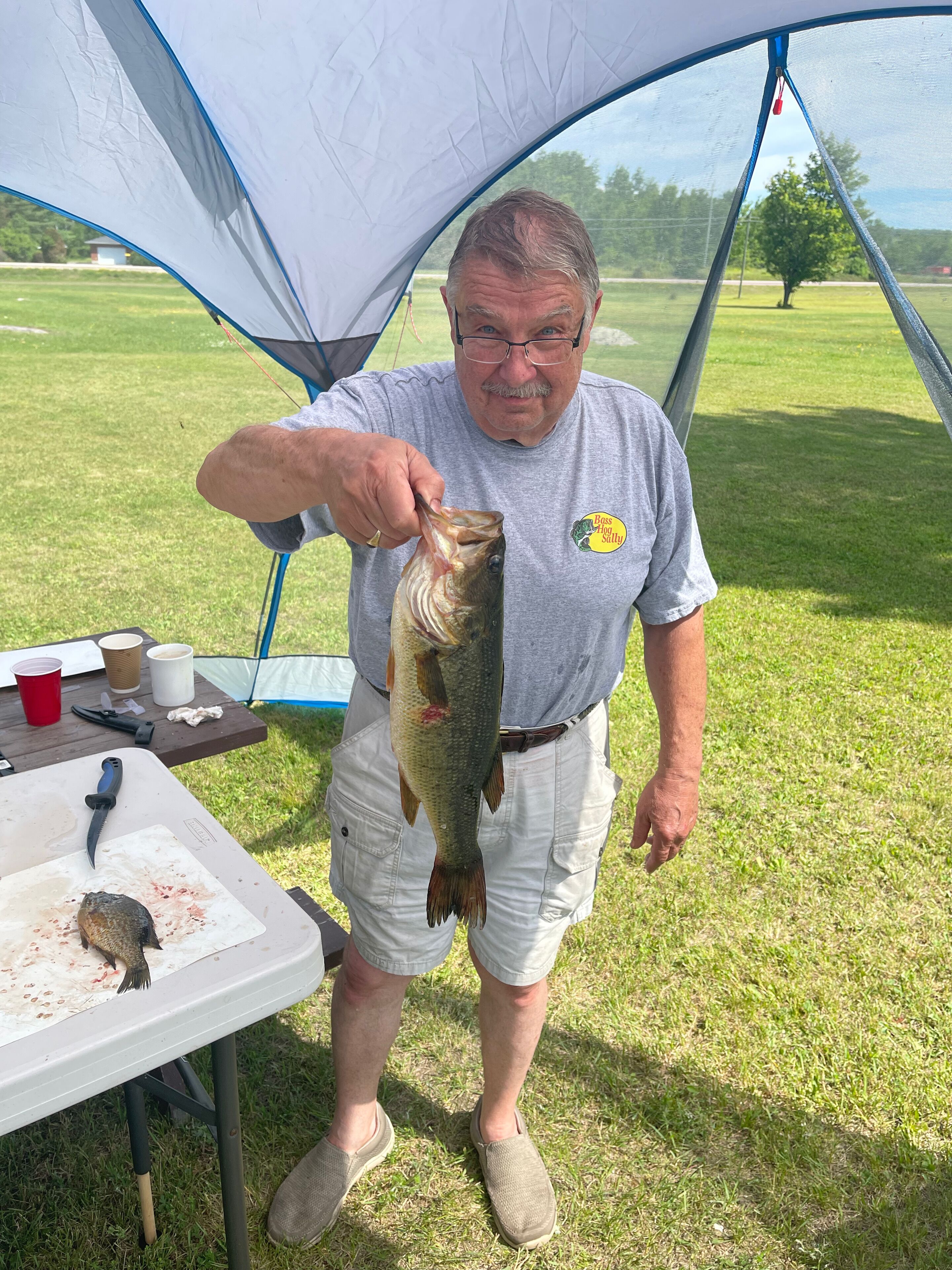 A man holding a fish near a tent.