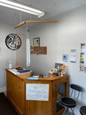 A reception desk with a wooden counter, a sign reading "Welcome Inn on Earl's Lake," a framed certificate, a key display, a phone, a notepad, and a "We Accept" card.