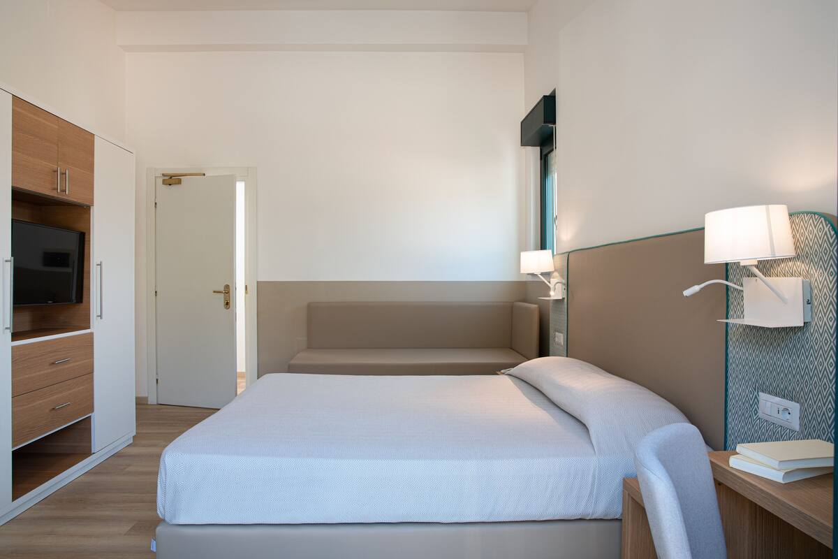 A neatly arranged bedroom with a bed, bedside table, lamp, and a TV in a built-in cabinet.