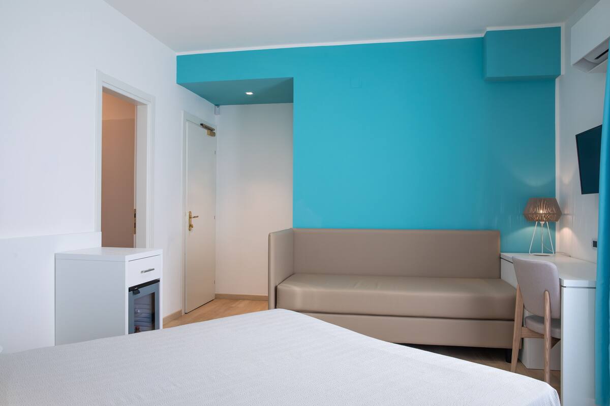 A bedroom with a bed, a desk, a chair, a wardrobe, and a door.