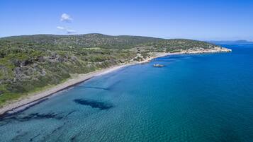 Un paysage côtier caractérisé par une eau d’un bleu limpide, une plage de sable et un relief vallonné.