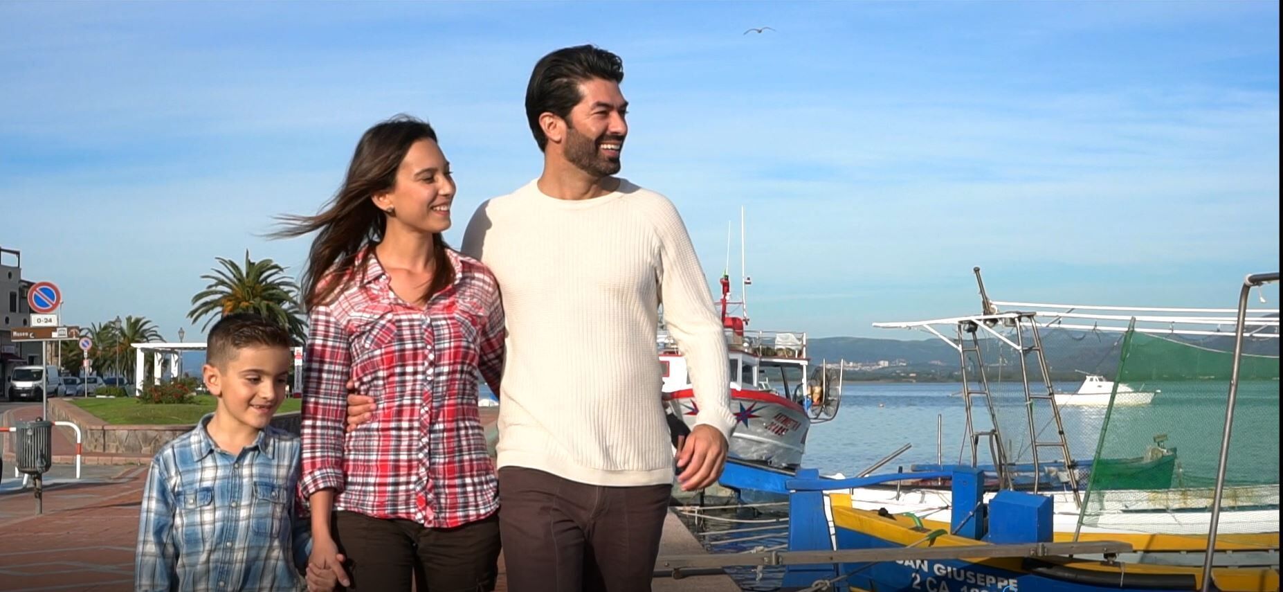A waterfront scene with a family walking by a dock with boats.