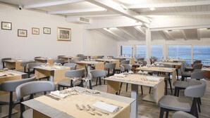 A dining area with tables set for service, framed pictures on the wall, and a view of the sea.