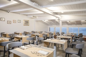 A dining area with tables set for service, framed pictures on the wall, and a view of the sea.