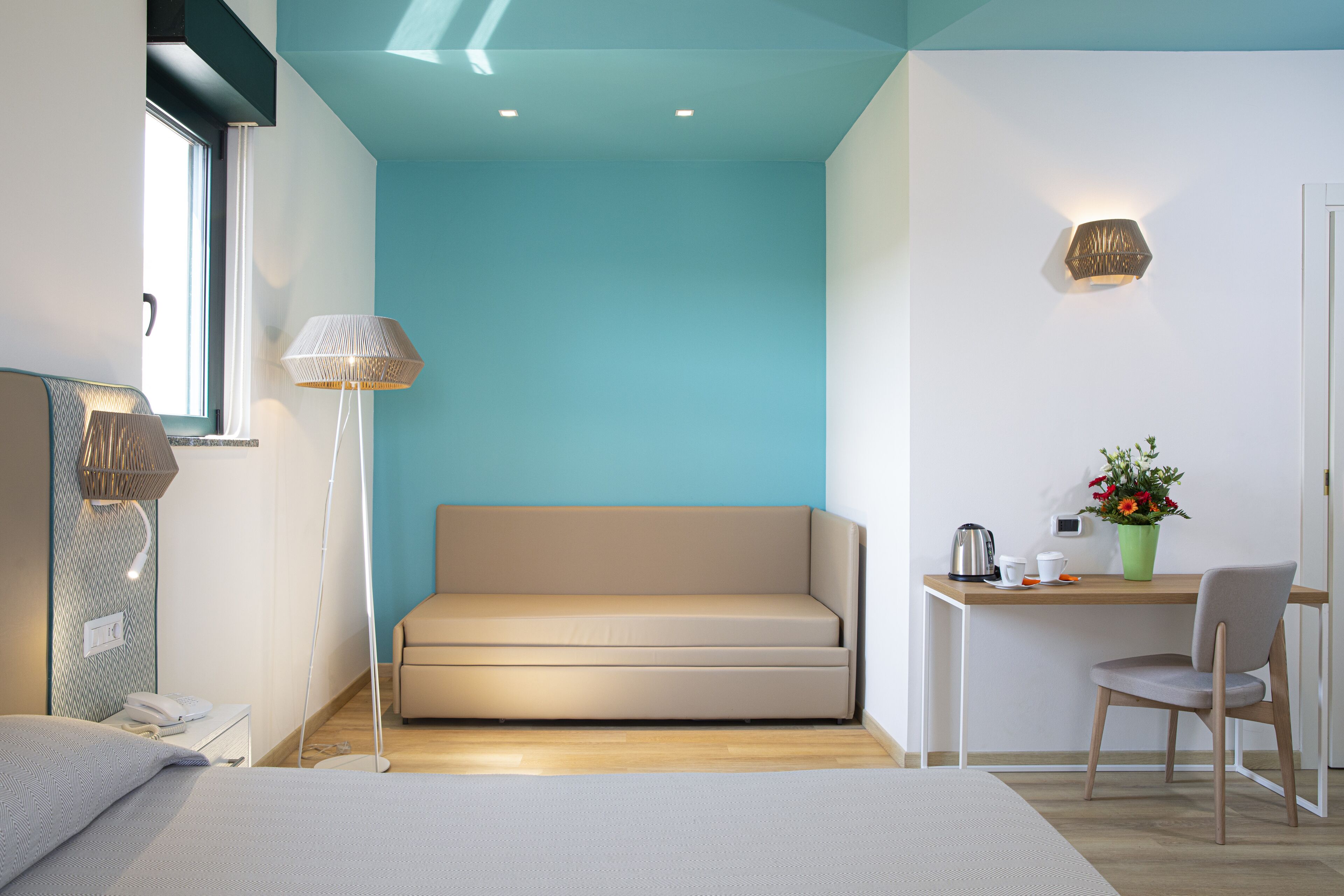 Una habitación moderna con un sofá, un escritorio con una silla, una lámpara y una mesita con una planta.