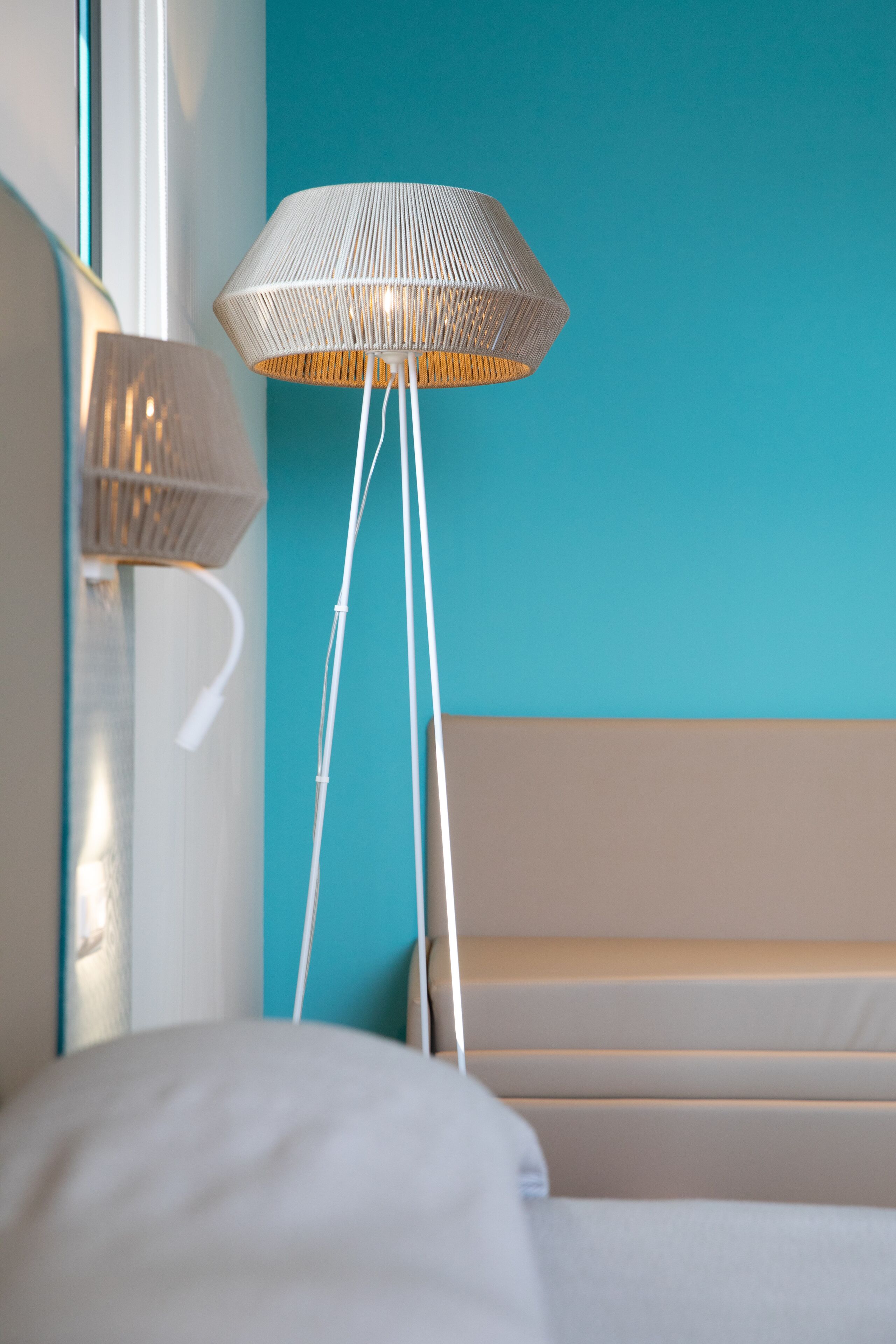 A modern room with a bed, a white lamp, and a floor lamp against a teal wall.
