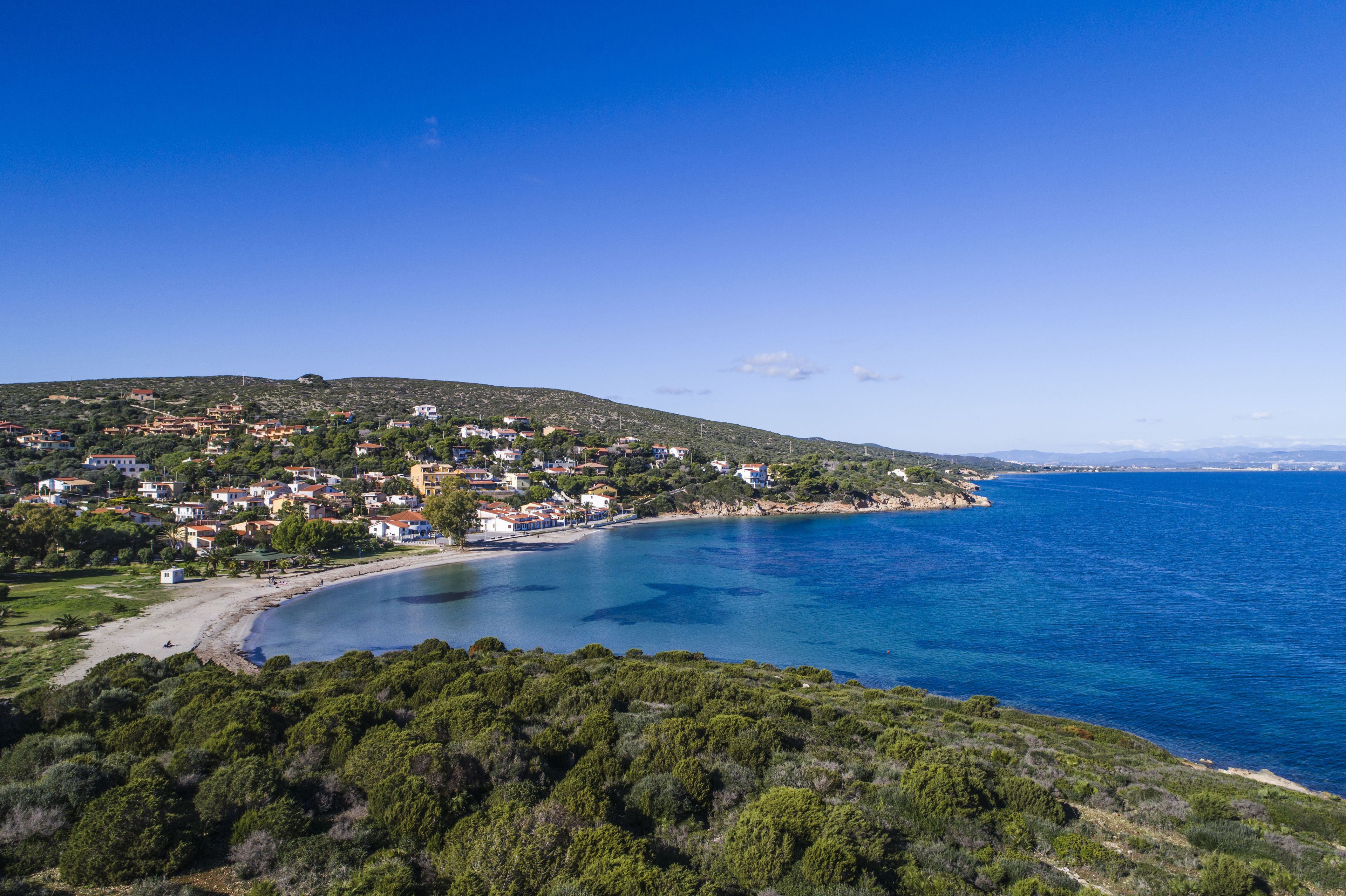 A coastal town with houses on a hillside overlooking a clear blue sea.
