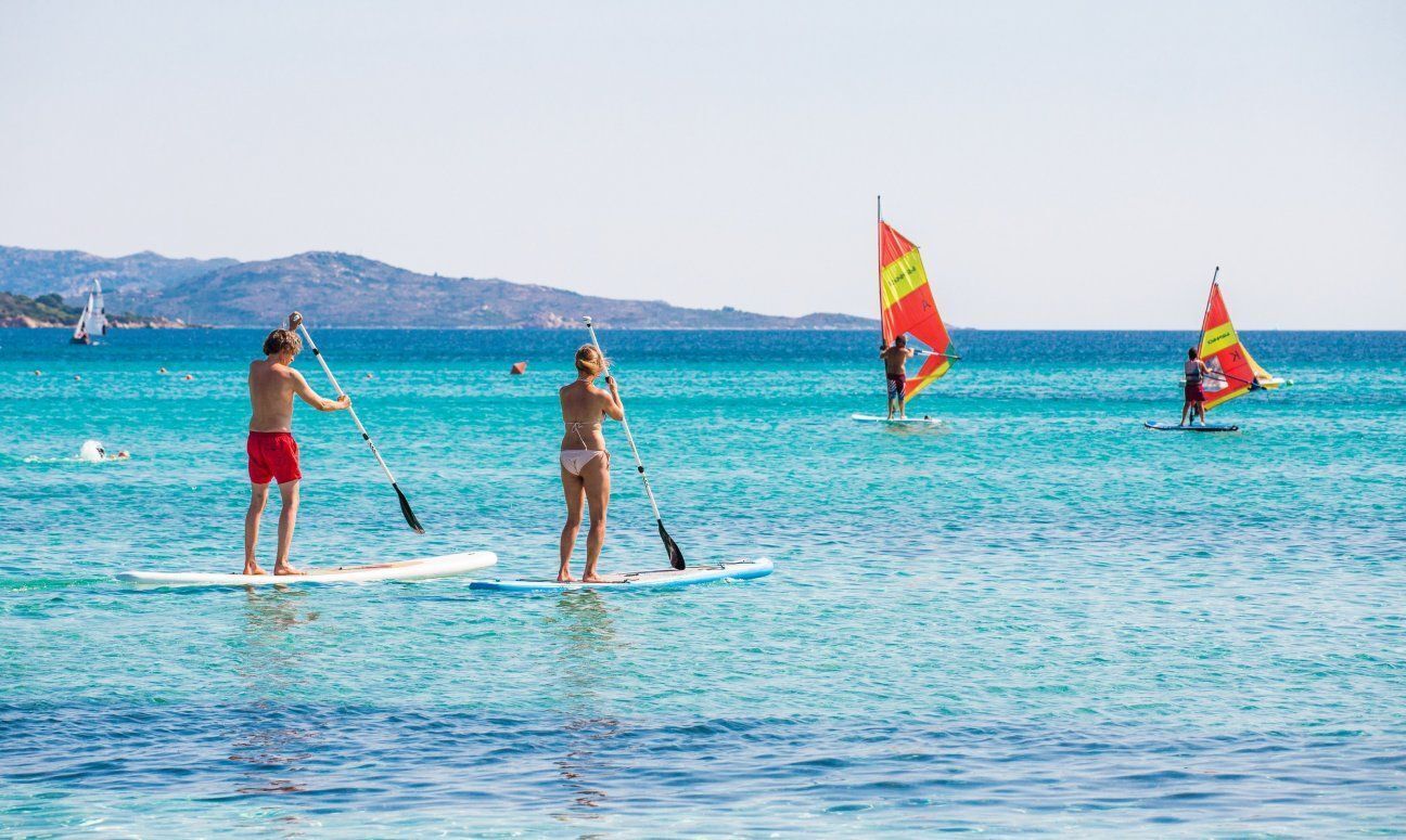 Three people paddleboarding on a calm sea with a clear sky and distant hills.