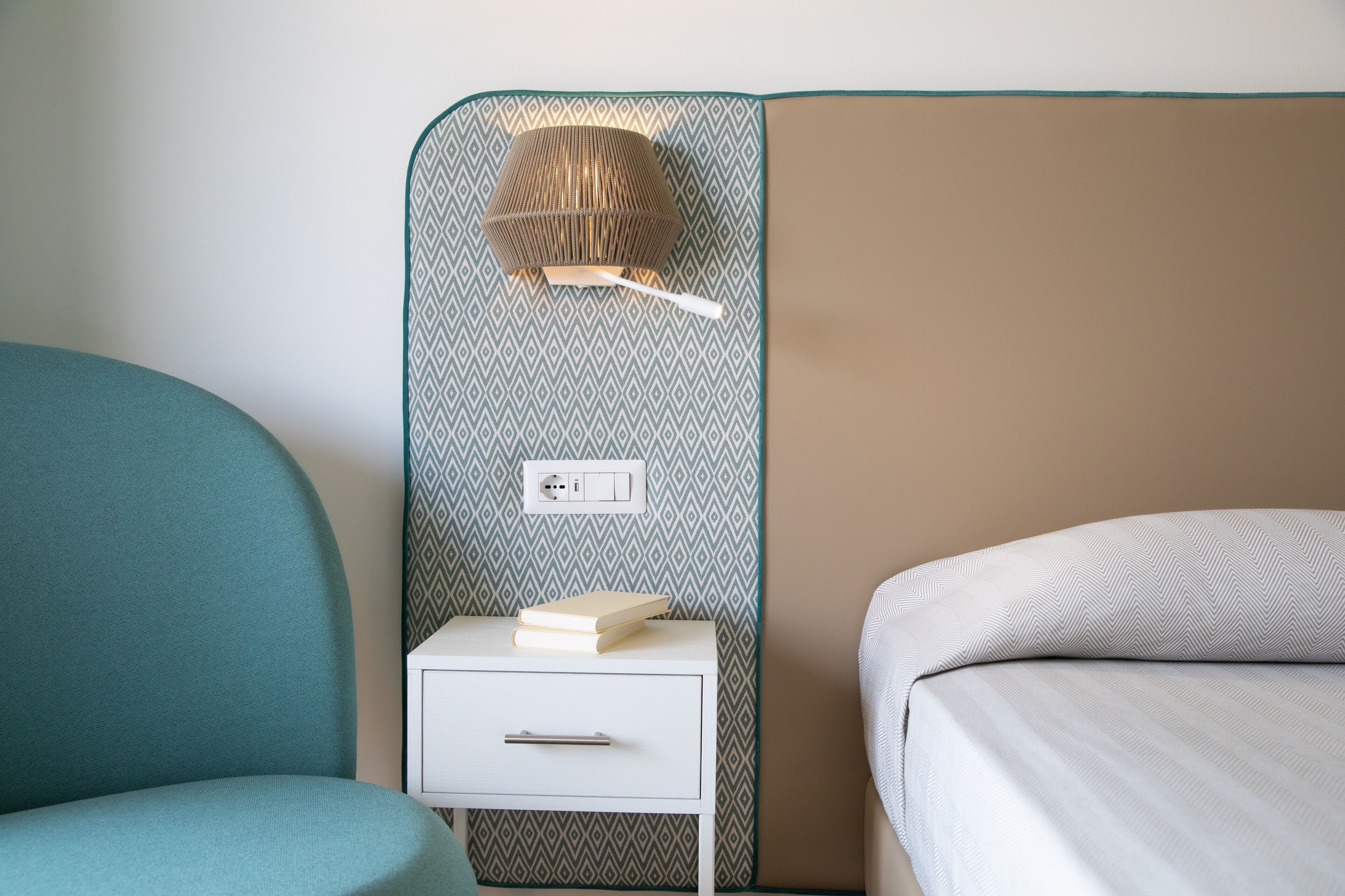 A bedroom with a bed, a nightstand with a lamp, and a chair.